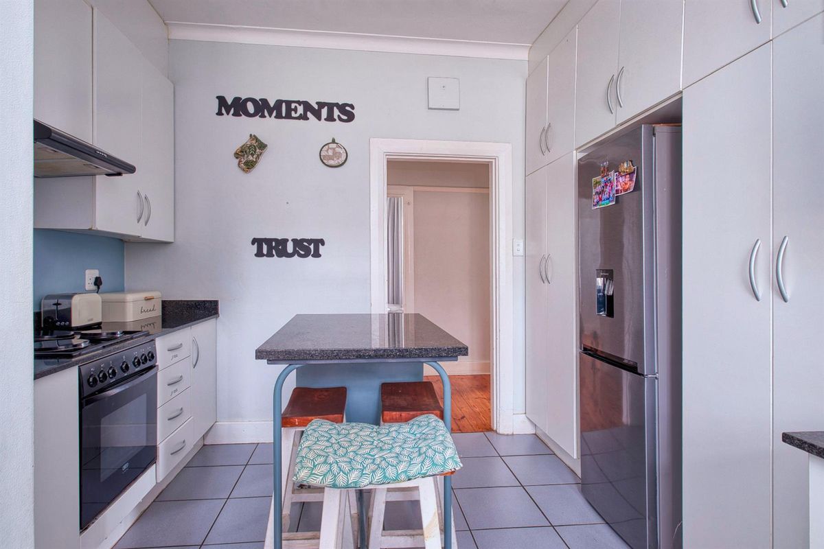 A functional kitchen featuring white built-in cabinetry, granite countertops, tiled flooring, and ample storage space with integrated pantry cupboards.