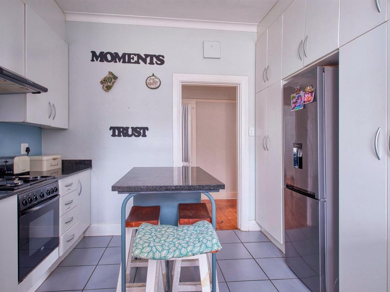 A functional kitchen featuring white built-in cabinetry, granite countertops, tiled flooring, and ample storage space with integrated pantry cupboards.