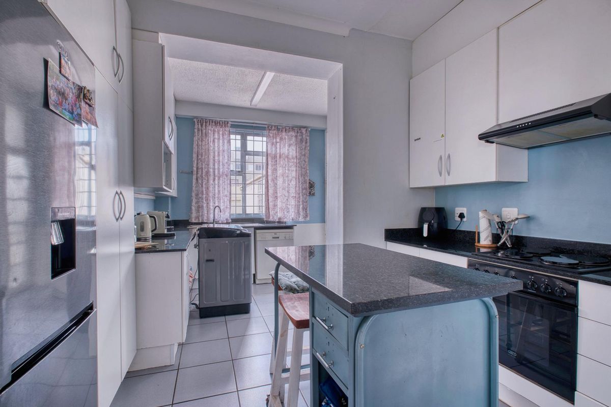 A functional kitchen featuring white cabinetry, dark granite countertops, a built-in oven with hob, and a separate laundry area with a sink.