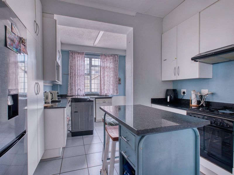 A functional kitchen featuring white cabinetry, dark granite countertops, a built-in oven with hob, and a separate laundry area with a sink.
