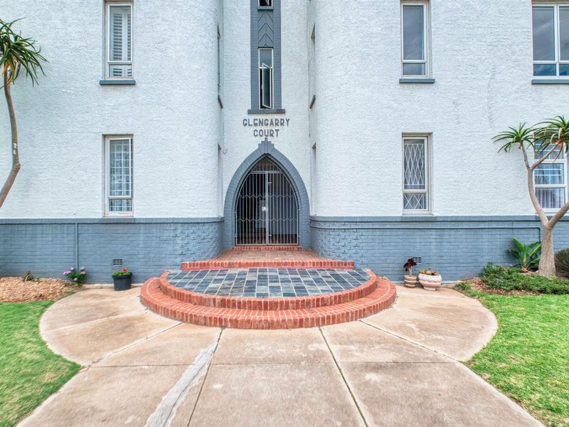 Front entrance of Glencarry Court apartment building featuring a distinctive arched security gate, brick steps, and a tiled landing.