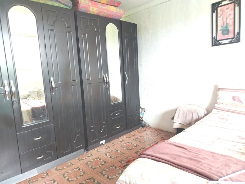 A bedroom featuring built-in dark wood wardrobes and patterned floor tiles, requiring cosmetic updates to improve the overall aesthetic and finish.