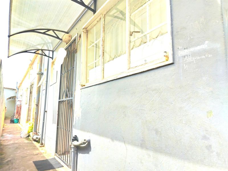 Side exterior view of the apartment building showing a security gate, metal window frames, and a protective awning over the walkway.