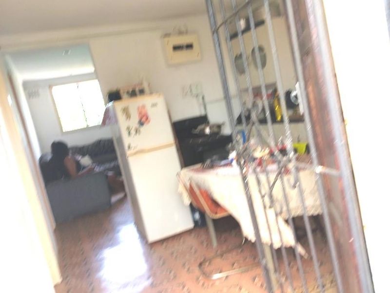 View through a security gate into an open plan living and kitchen area featuring tiled flooring and an electrical distribution board.