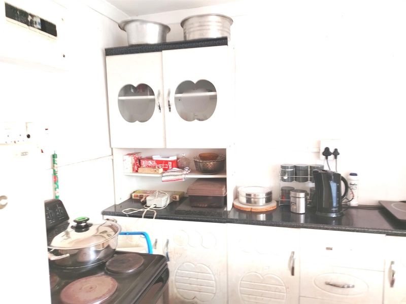 A compact kitchen featuring white cabinetry, dark countertops, and a built-in electric stove, requiring cosmetic updates to modernize the space.