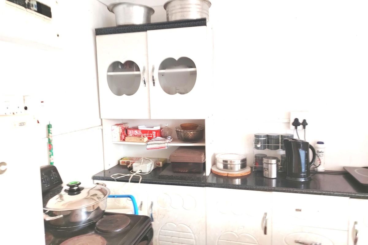 A compact kitchen featuring white cabinetry, dark countertops, and a built-in electric stove, requiring cosmetic updates to modernize the space.
