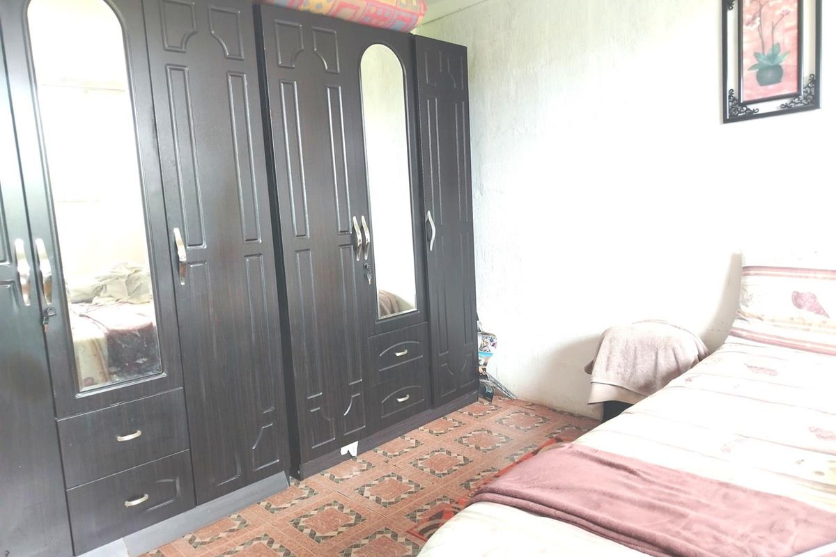 A bedroom featuring built-in dark wood wardrobes and patterned floor tiles, requiring cosmetic updates to improve the overall aesthetic and finish.