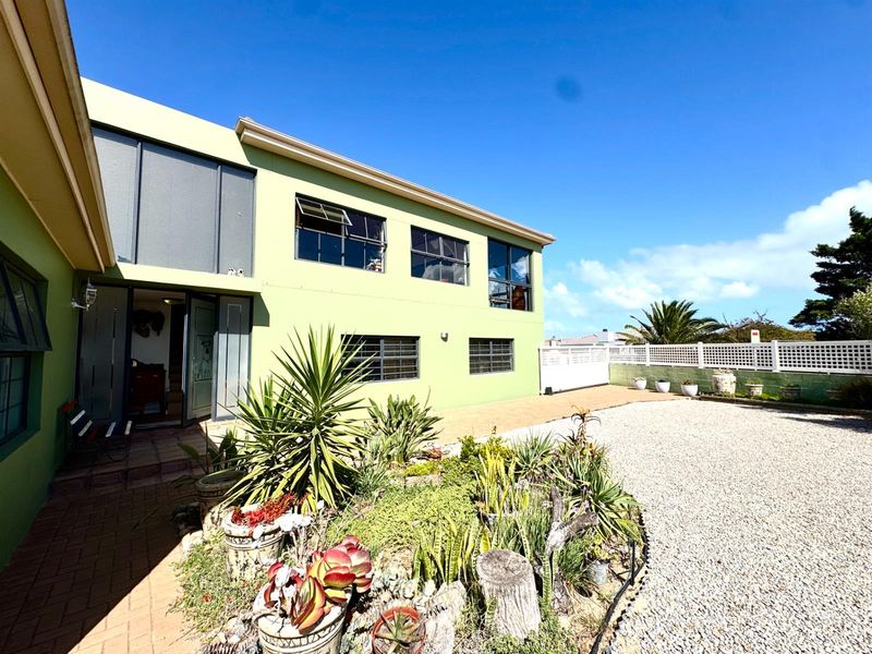 Rear exterior view of the property featuring a paved patio area, gravel driveway, and established garden beds against a two-story building facade.