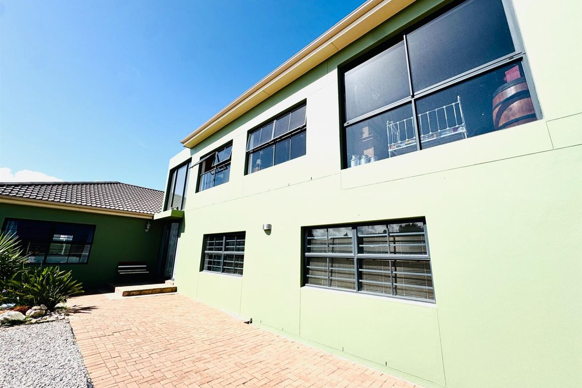 A view of the rear exterior facade featuring light green painted walls, brick paving, and aluminium-framed windows with security bars.