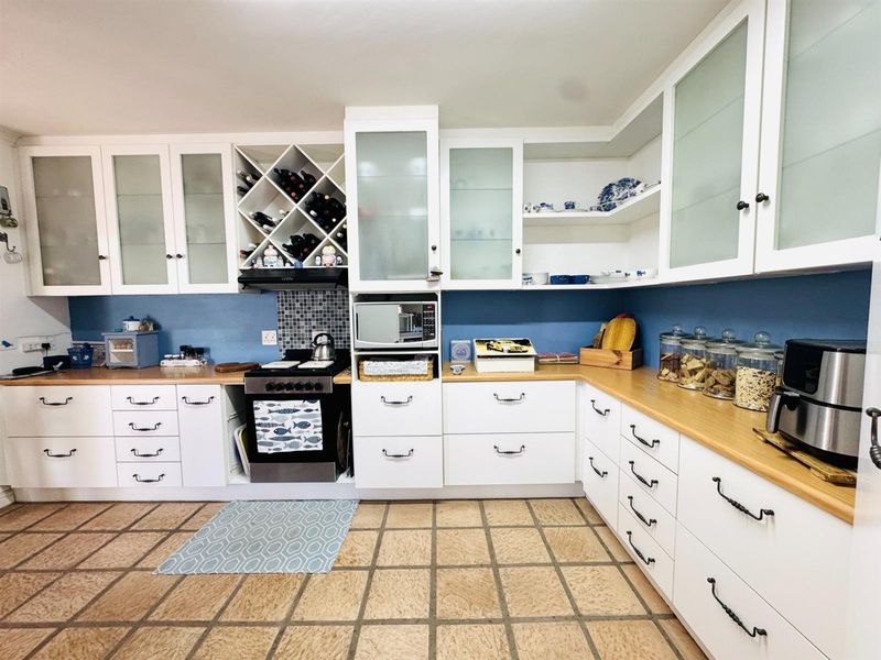 A functional kitchen featuring white cabinetry, wooden countertops, a built-in wine rack, and tiled flooring with a blue splashback.