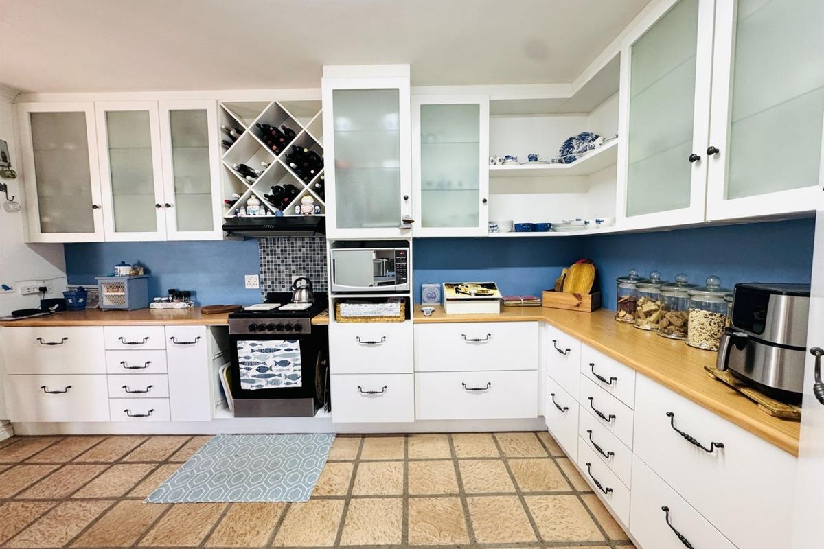 A functional kitchen featuring white cabinetry, wooden countertops, a built-in wine rack, and tiled flooring with a blue splashback.
