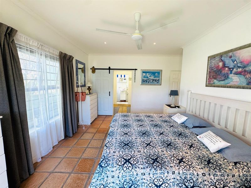 Spacious bedroom featuring terracotta floor tiles, a ceiling fan, and a sliding barn door leading to an en-suite bathroom.