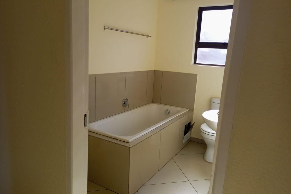 A functional bathroom featuring a built-in bathtub, pedestal basin, and toilet, with neutral wall and floor tiling throughout.