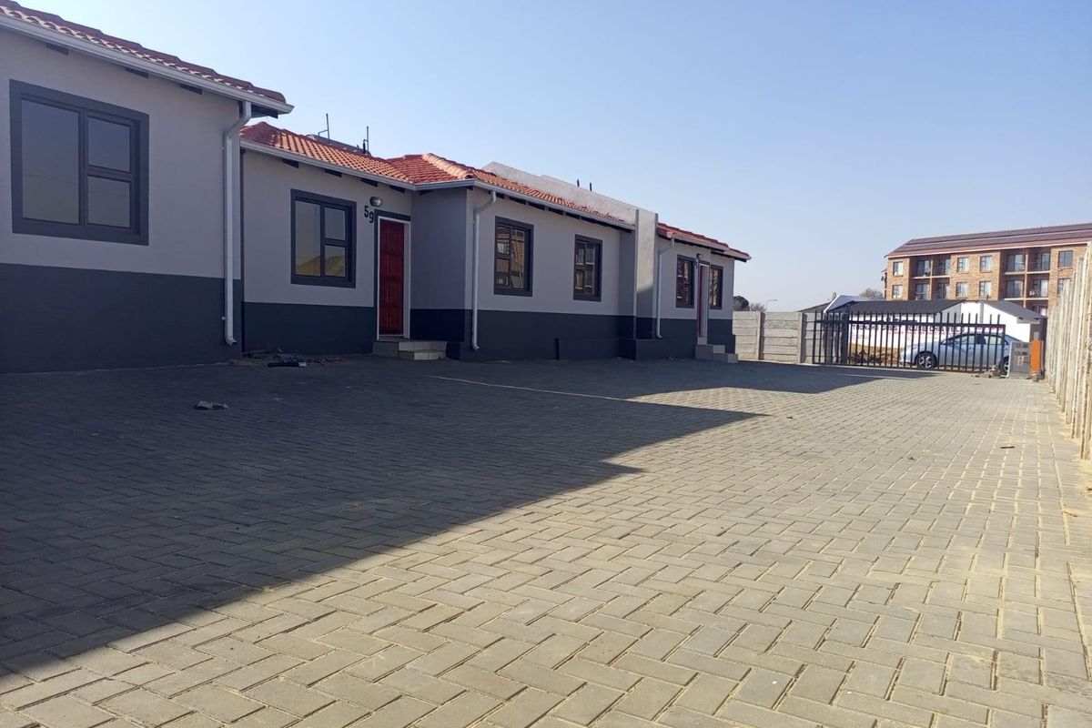 Front view of a townhouse complex featuring a paved driveway, tiled roofing, and secure gated access.