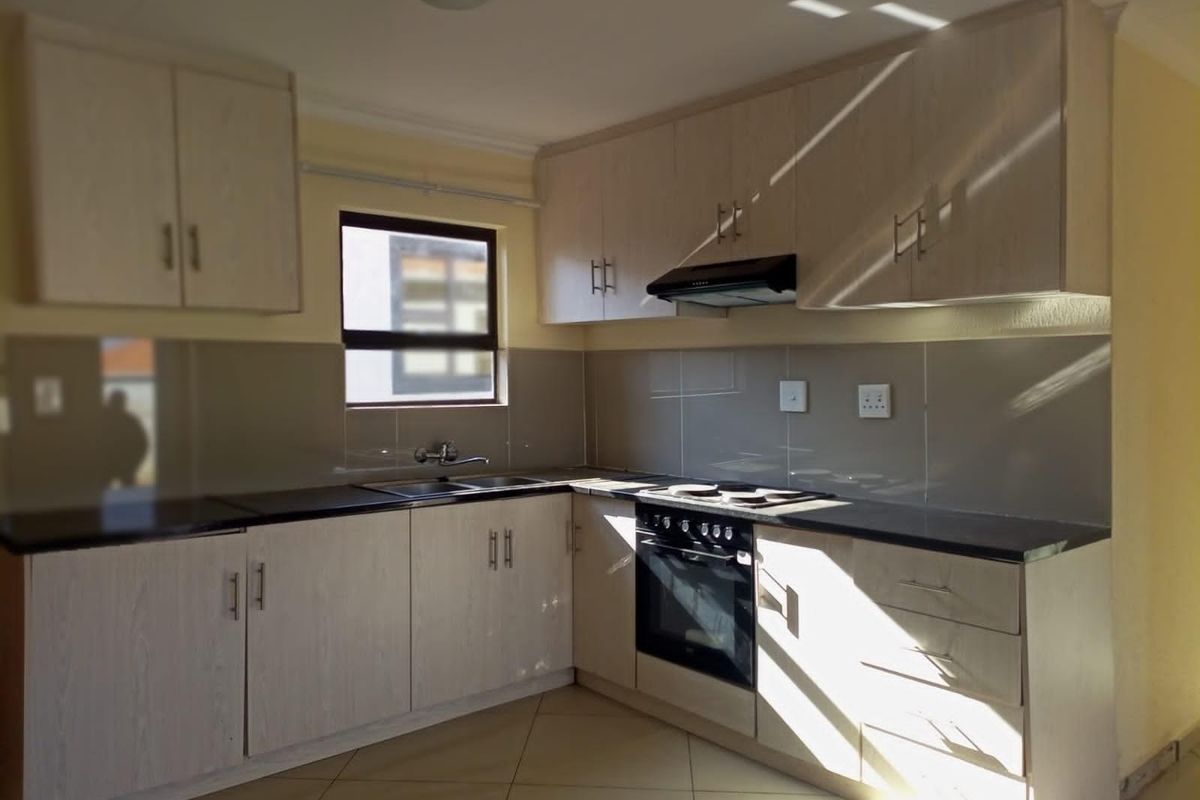 A clean, modern kitchen featuring light wood-finish cabinetry, dark granite countertops, built-in oven, hob, and extractor fan with neutral tiled backsplash and flooring.