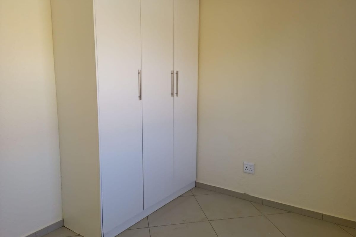 A clean, empty bedroom featuring neutral tiled flooring and a modern white built-in wardrobe with sleek handles.