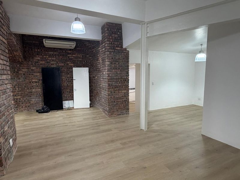 Open plan retail or office space featuring exposed brick feature walls, wood-look laminate flooring, and integrated ceiling lighting.