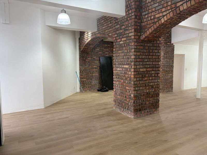 Open plan retail space featuring exposed brick columns, arched brick detailing, and modern light-toned wood-look flooring.
