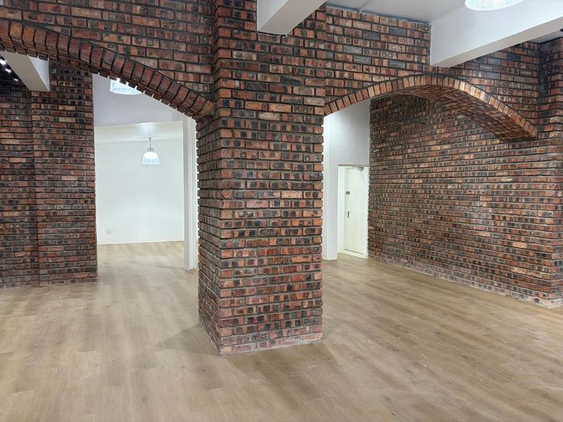 Spacious open-plan retail area featuring exposed brick columns, arched architectural details, and modern light-toned wood-look flooring.