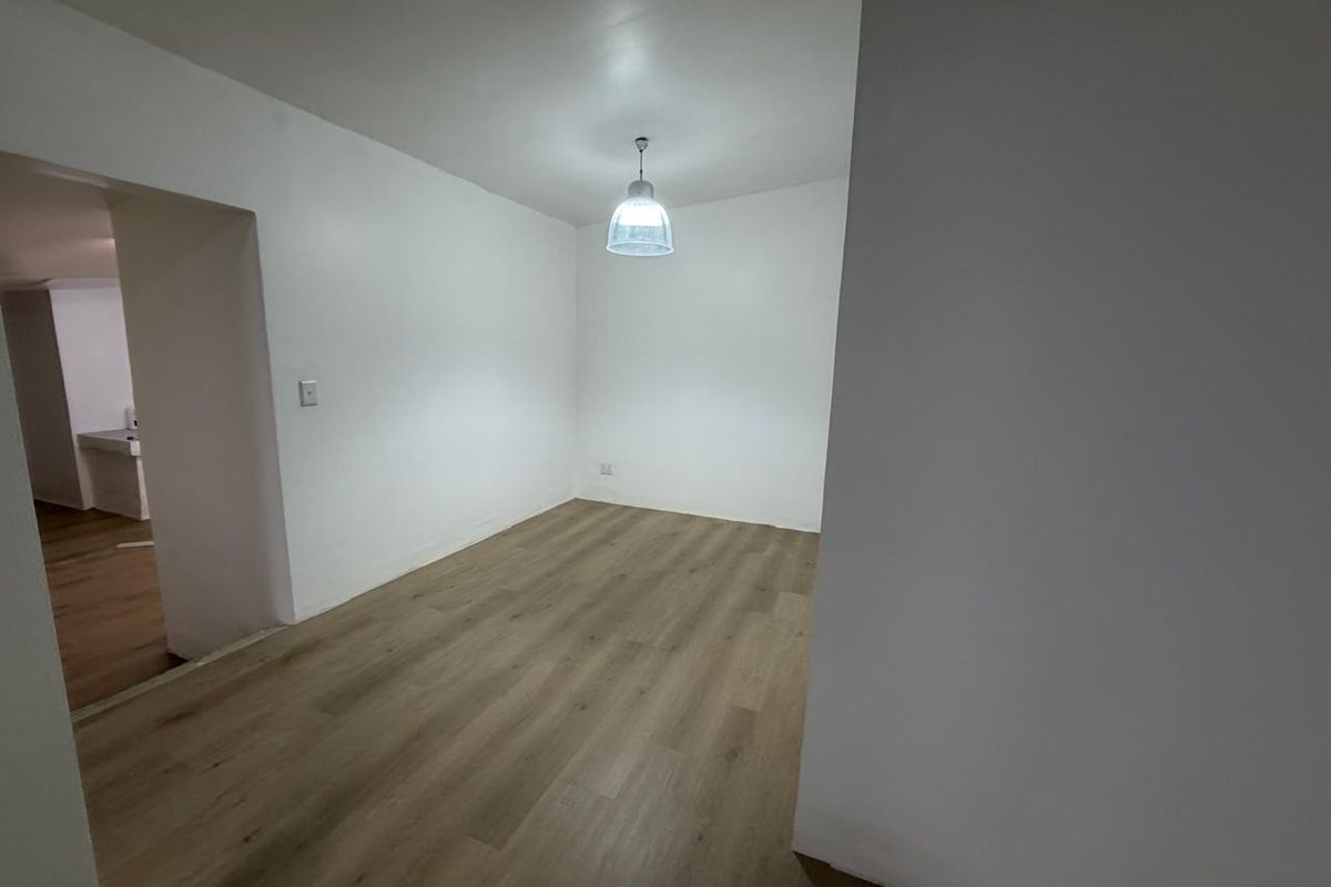 A bright, empty interior space featuring modern wood-look laminate flooring and a central pendant light fixture, offering a clean and versatile layout.