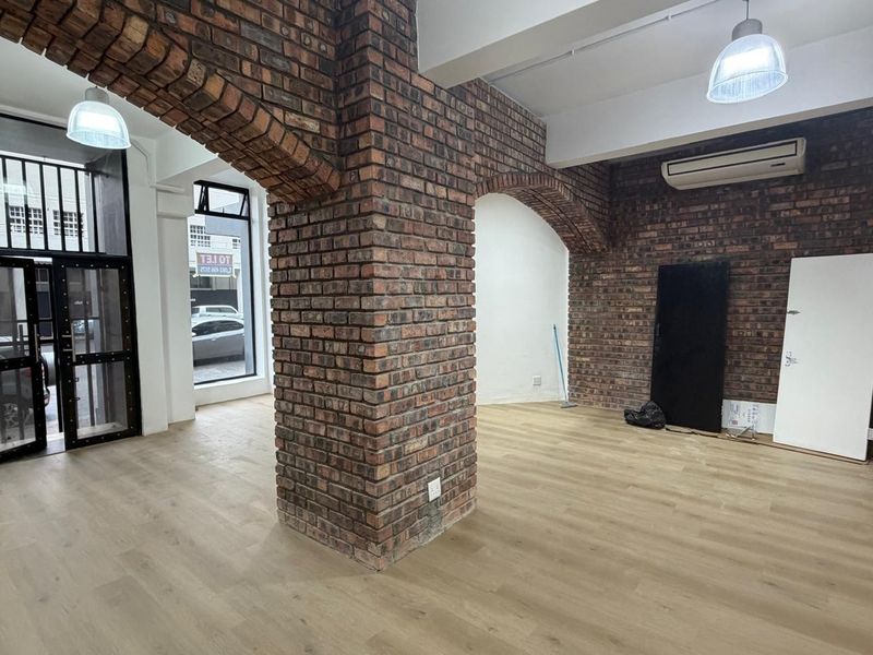 Open plan retail space featuring exposed brick archways, wood-look flooring, and modern pendant lighting.