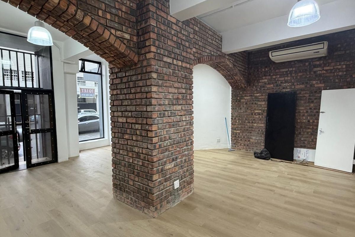 Open plan retail space featuring exposed brick archways, wood-look flooring, and modern pendant lighting.