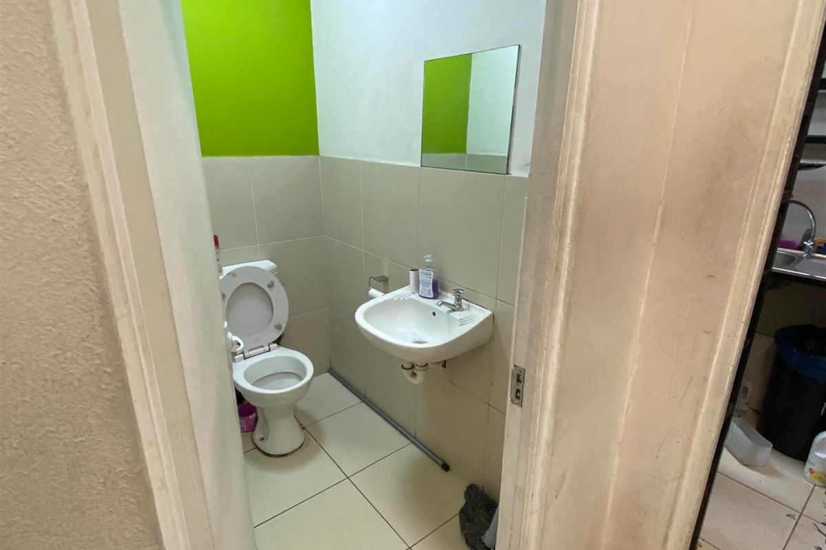 A compact functional bathroom featuring a wall-mounted basin, toilet, and tiled flooring with a bright accent wall.
