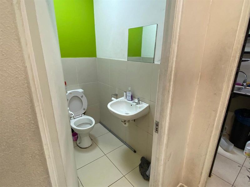 A compact functional bathroom featuring a wall-mounted basin, toilet, and tiled flooring with a bright accent wall.