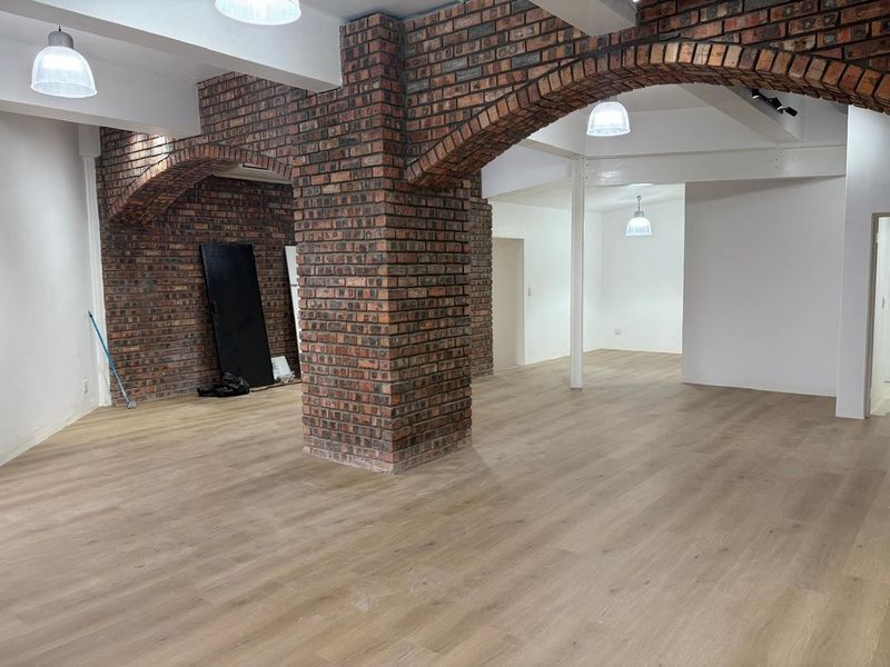 Spacious open-plan retail area featuring exposed brick columns, decorative brick arches, and modern light-toned wood-look flooring.