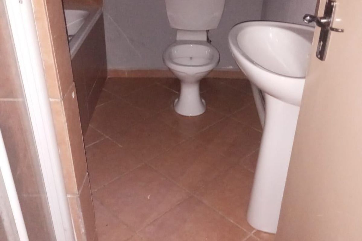 A functional bathroom featuring a pedestal sink, toilet, and bathtub with tiled flooring and basic wall finishes.
