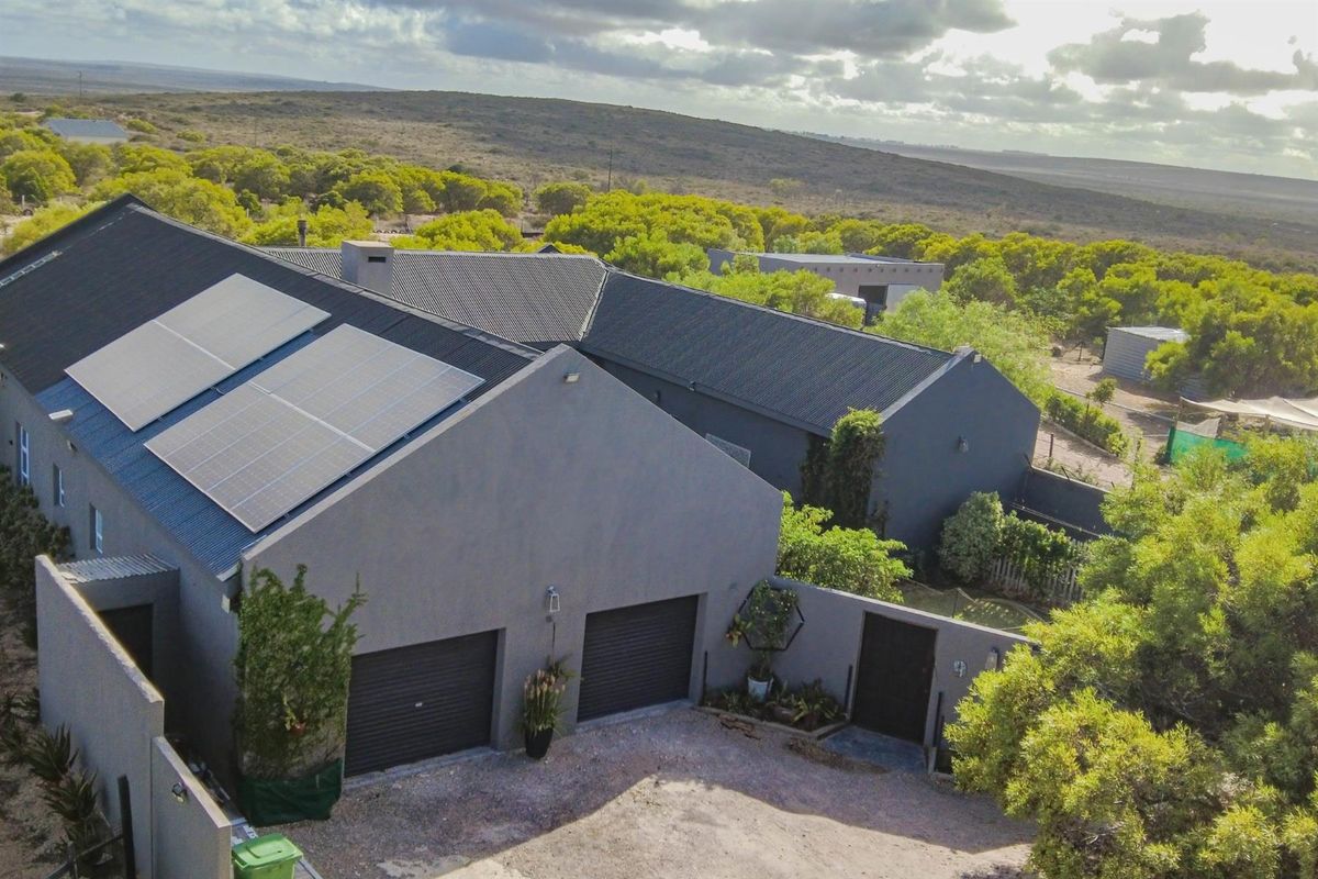 Aerial view of a modern house featuring a dark grey exterior, double garage with roller doors, and roof-mounted solar panels set in a natural landscape.