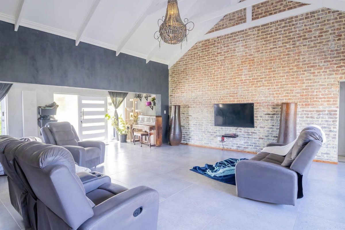 Spacious living room featuring a high vaulted ceiling with exposed rafters, a striking exposed brick feature wall, and modern tiled flooring.