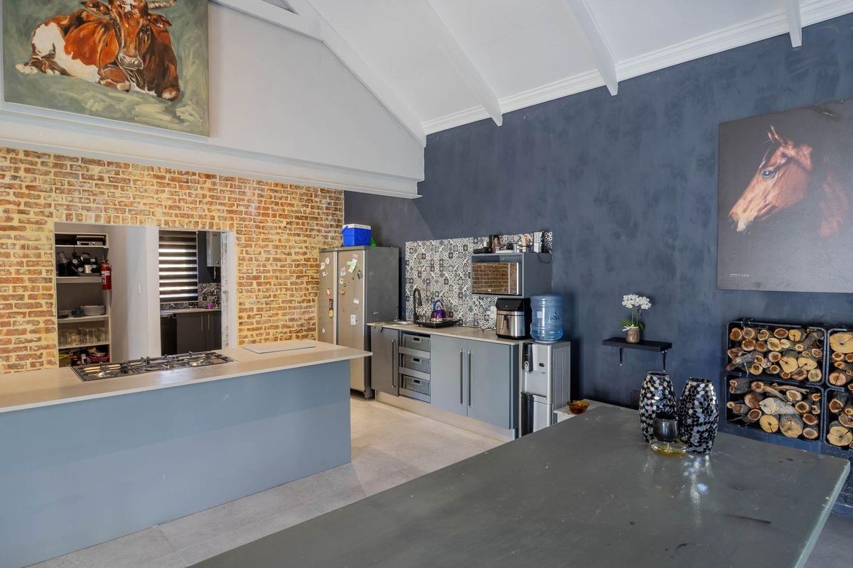 Spacious kitchen featuring a vaulted ceiling, exposed brick wall, central island with gas hob, and modern cabinetry with a decorative tiled backsplash.