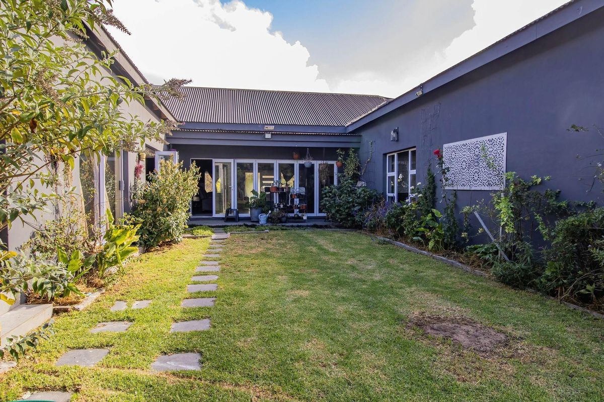 A private rear courtyard featuring a central lawn, stone pathway, and large folding glass doors providing seamless access to the home's interior living spaces.
