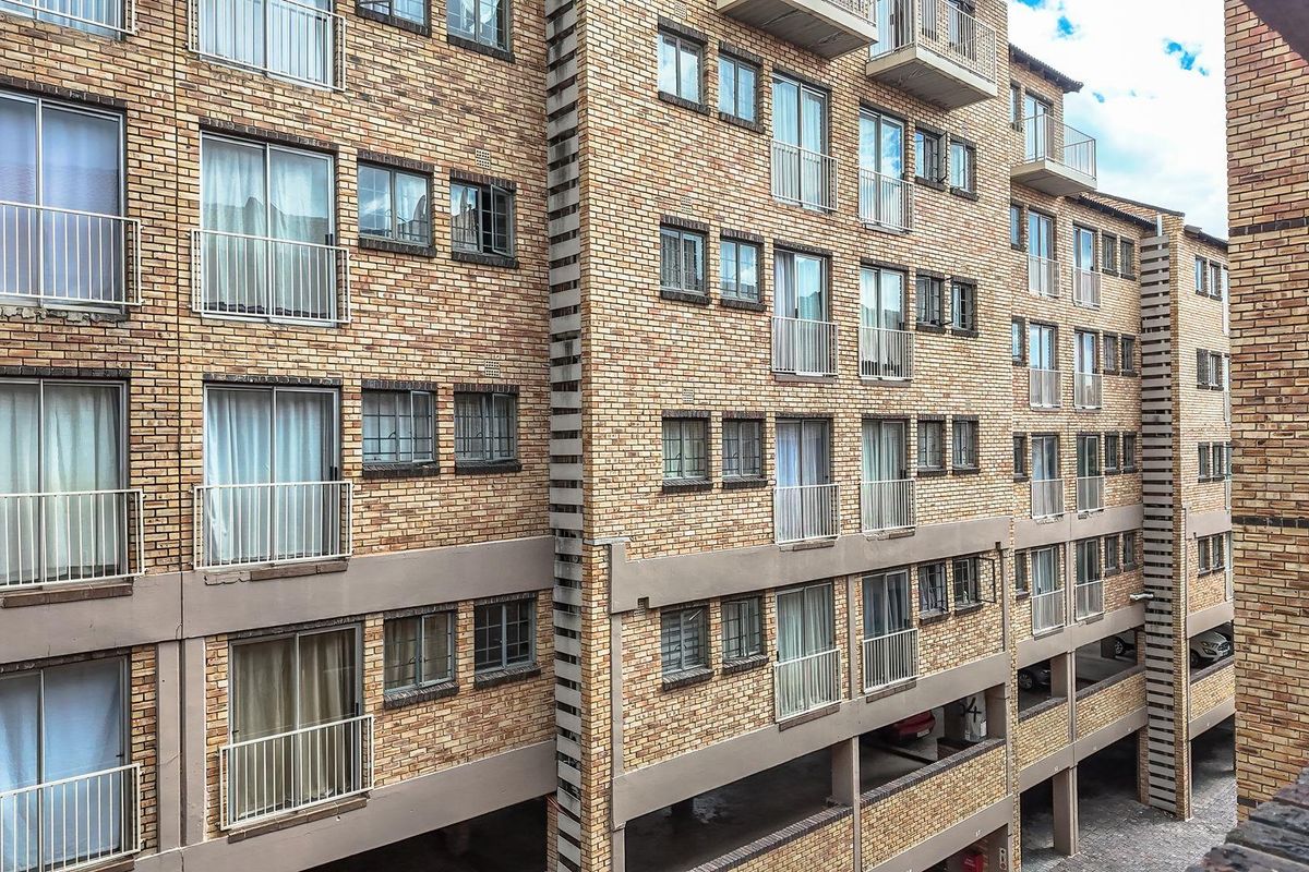 Exterior view of a multi-story apartment building featuring face brick facade, multiple balconies with metal railings, and ground-level undercover parking.