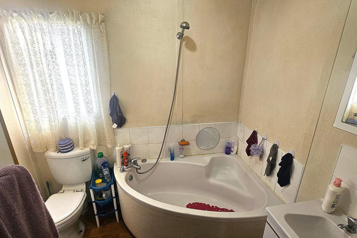 A dated bathroom featuring a corner bathtub with a handheld shower attachment, a standard toilet, and a vanity basin.