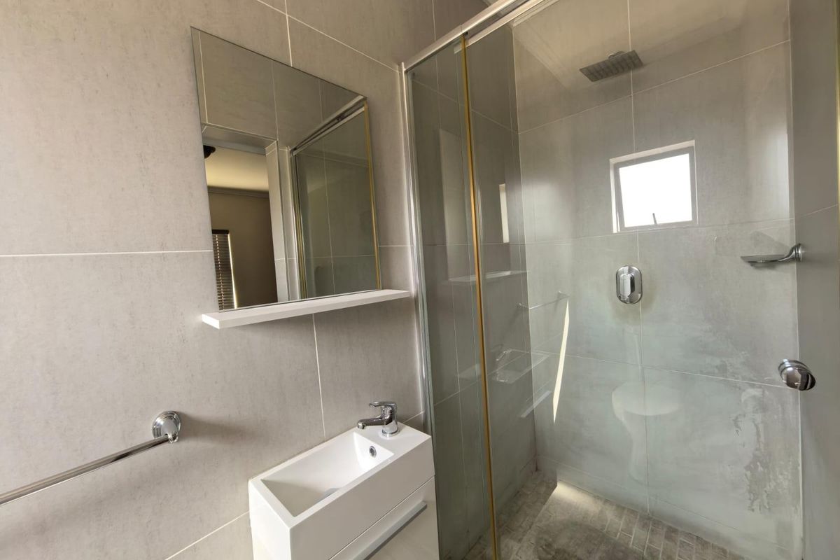 Modern bathroom featuring a glass-enclosed shower with rainfall showerhead, wall-mounted vanity basin, and neutral floor-to-ceiling tiling.