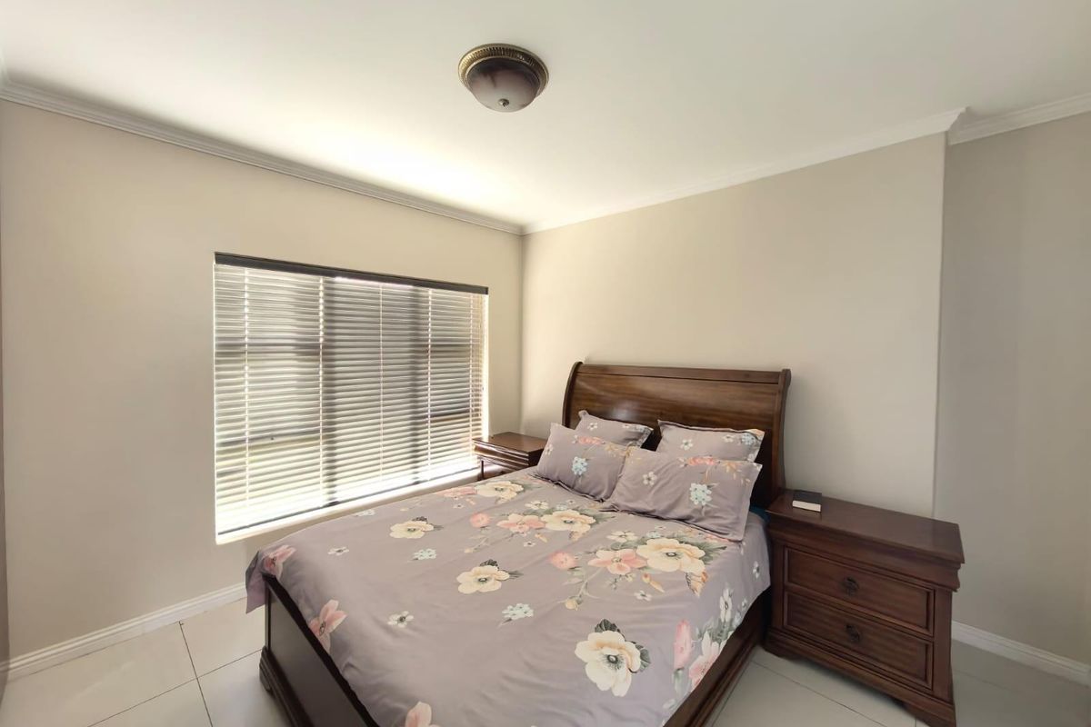 A well-maintained bedroom featuring neutral wall tones, tiled flooring, and a window fitted with horizontal blinds.