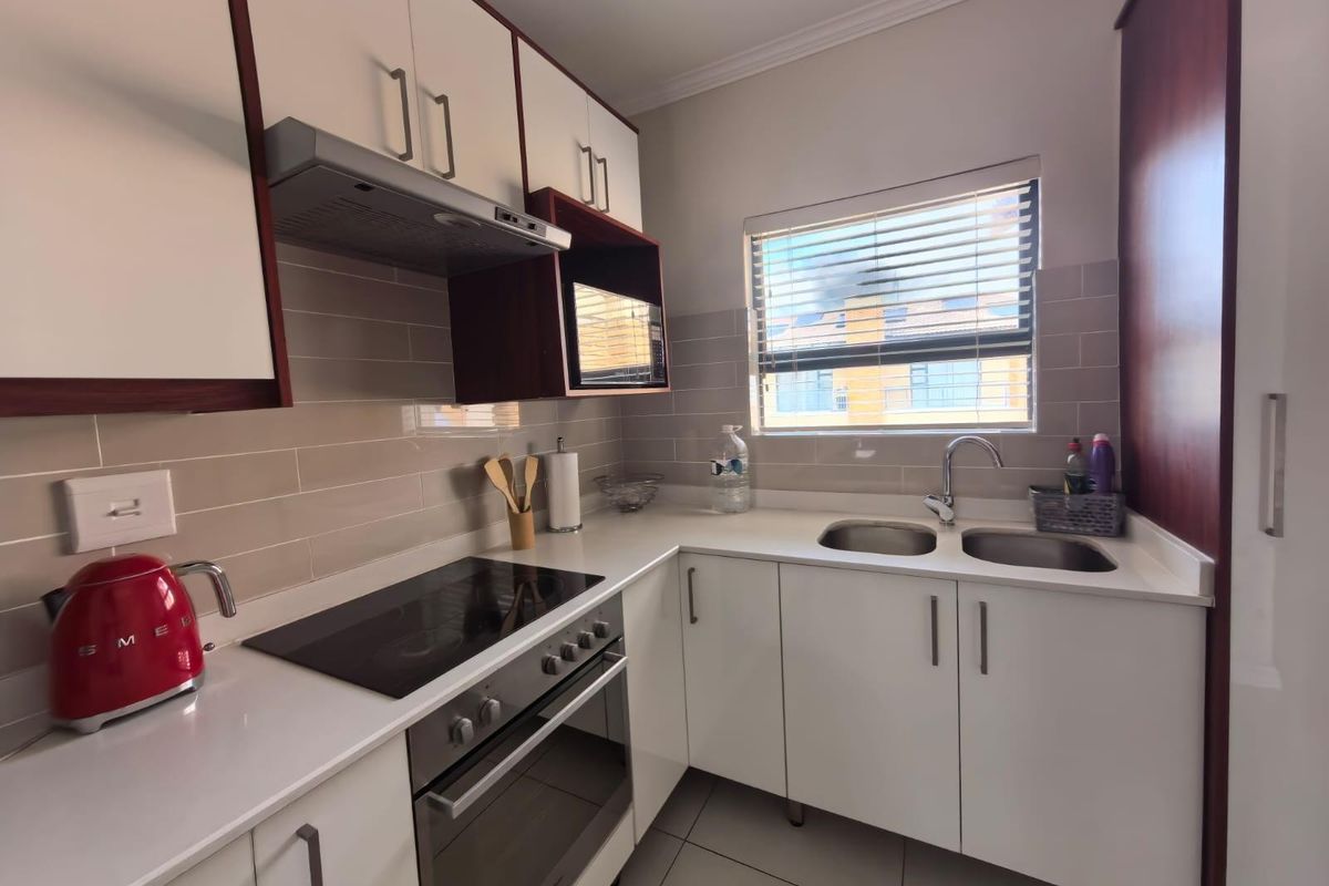A compact, modern kitchen featuring white cabinetry, stone countertops, a built-in electric oven, hob, extractor fan, and a double-basin sink.