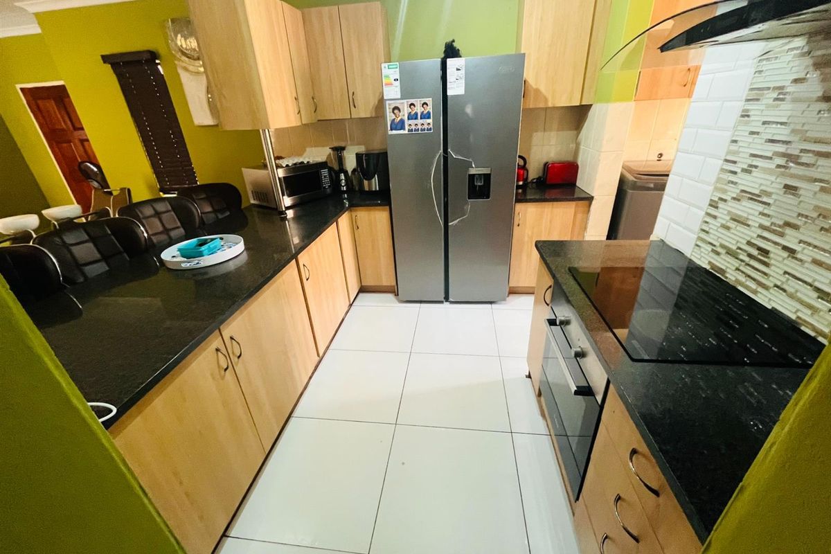 A functional kitchen featuring light wood cabinetry, dark granite countertops, a built-in oven, glass hob, and a modern extractor fan.