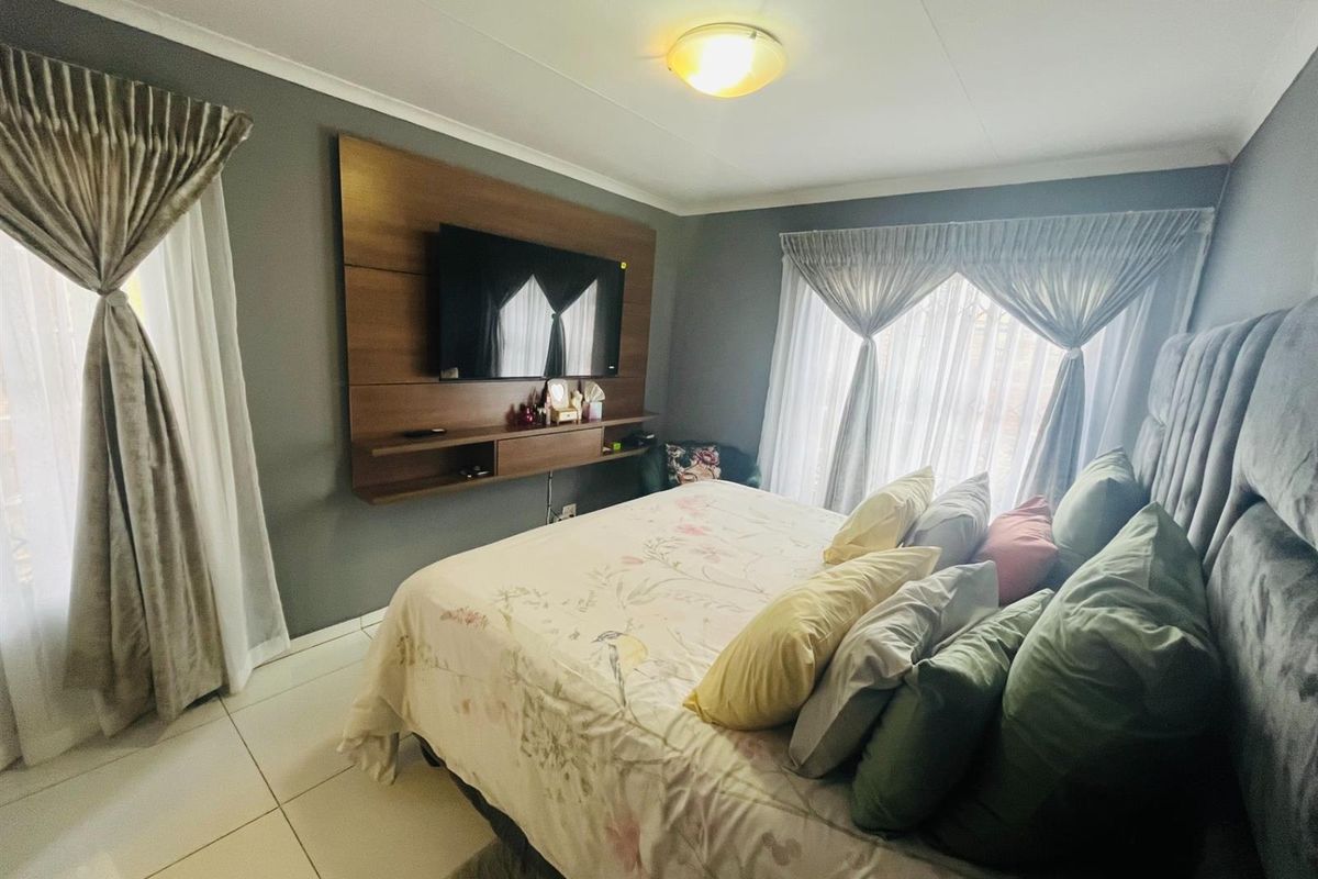 A well-maintained bedroom featuring tiled flooring, a built-in wooden media console, and large windows with curtain treatments.