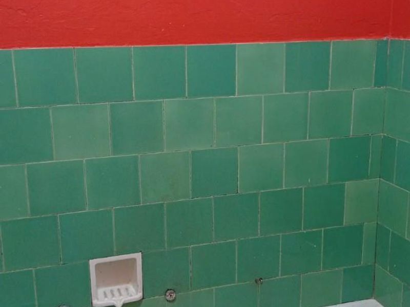 A dated bathroom featuring a bathtub with integrated faucet, green wall tiling, and a built-in soap dish, requiring cosmetic updates and maintenance.