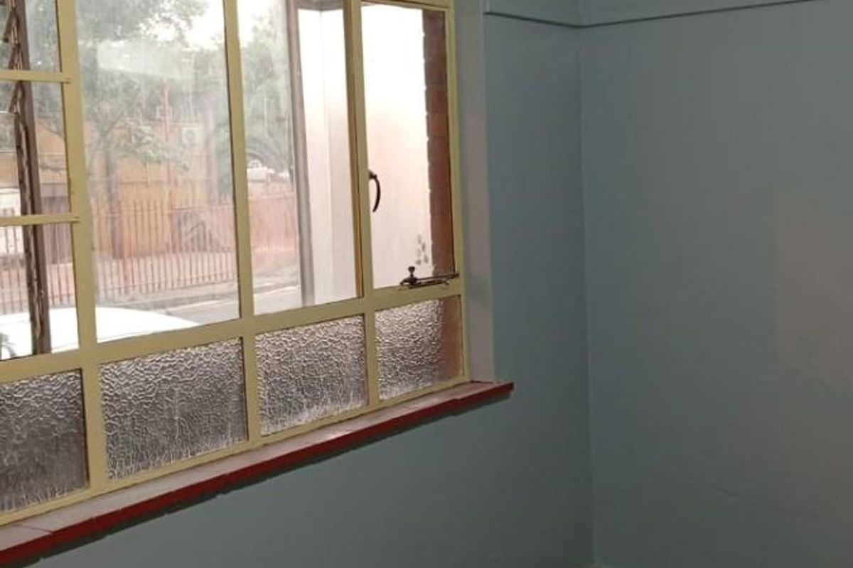 An empty bedroom featuring original parquet flooring, large multi-pane windows with yellow frames, and light blue painted walls.