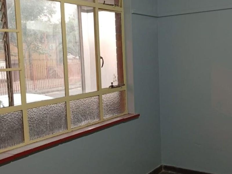 An empty bedroom featuring original parquet flooring, large multi-pane windows with yellow frames, and light blue painted walls.