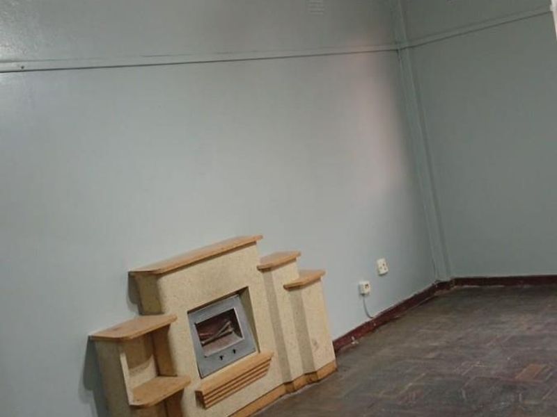 An empty living room featuring original parquet flooring, a built-in fireplace, and a traditional ceiling light fixture.