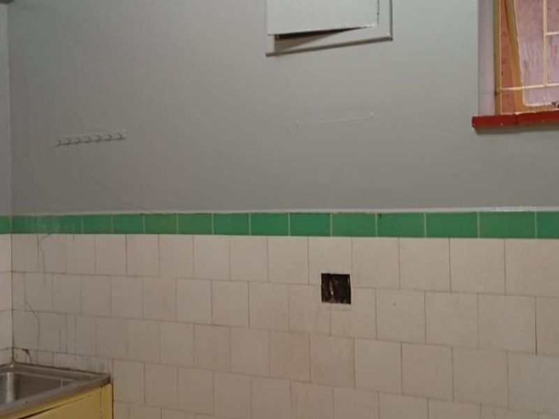 A functional kitchen area featuring tiled splashbacks, a stainless steel sink, and built-in cabinetry, requiring cosmetic updates to modernize the space.