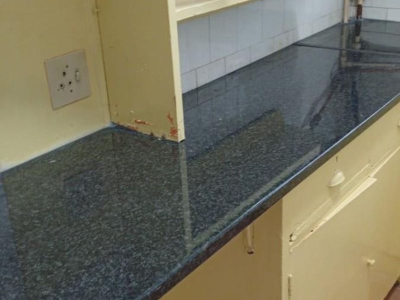 A dated kitchen area featuring dark granite countertops, yellow cabinetry, and exposed plumbing fixtures against a tiled backsplash.