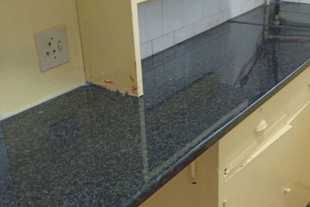 A dated kitchen area featuring dark granite countertops, yellow cabinetry, and exposed plumbing fixtures against a tiled backsplash.