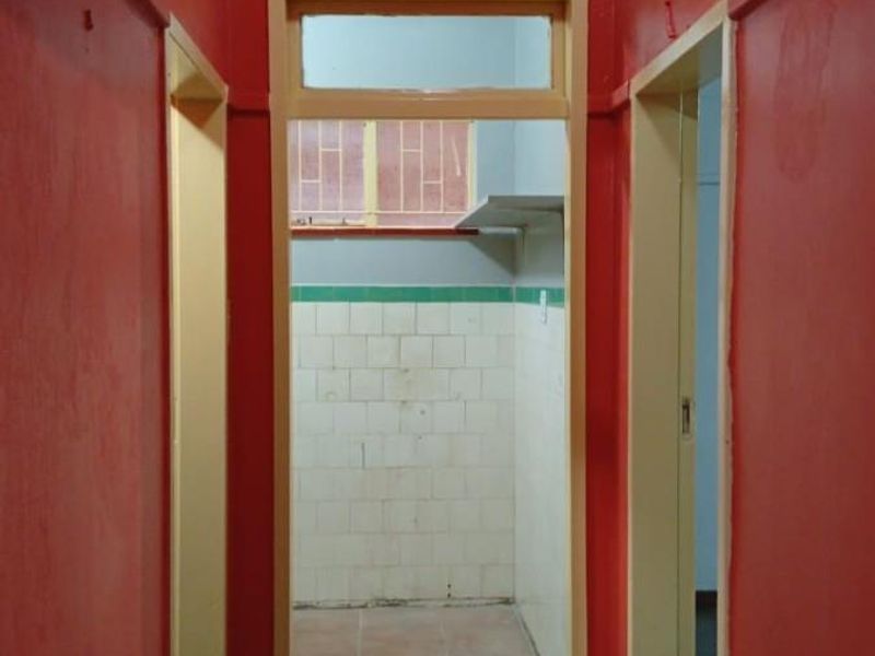 A narrow interior hallway with red painted walls leading into a tiled utility or kitchen area with vintage wall tiling.