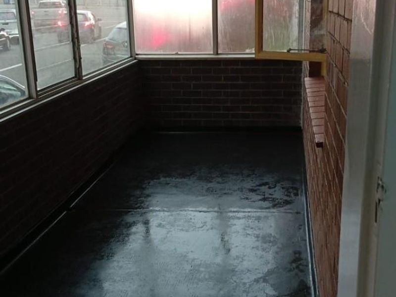 An enclosed balcony or sunroom featuring exposed brick walls, large glass windows, and a dark painted concrete floor.